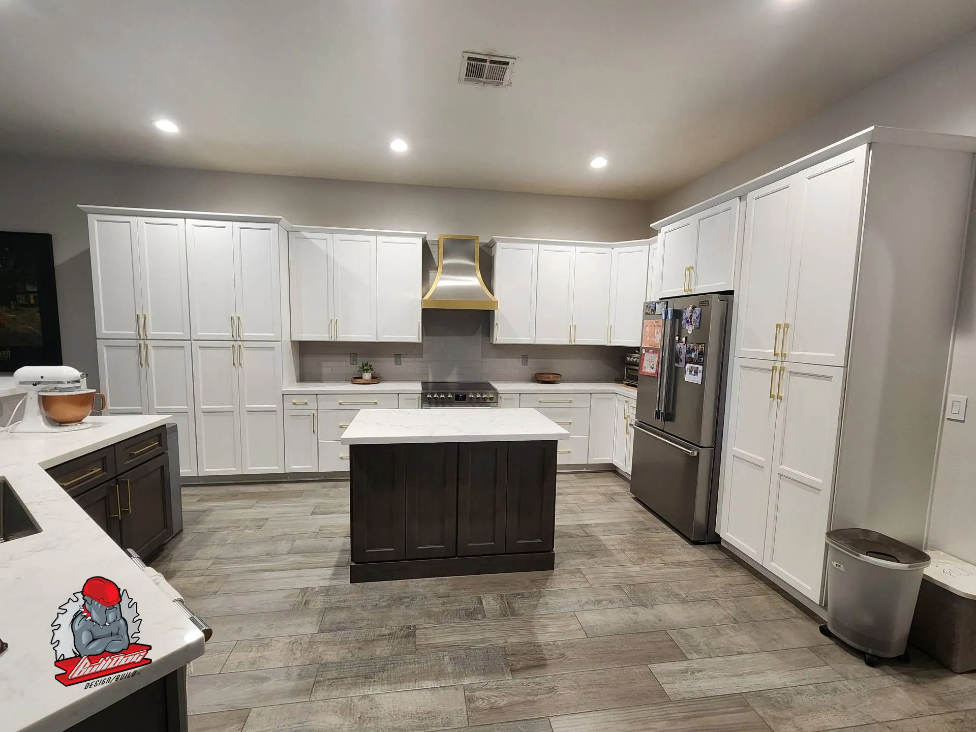 Bright white kitchen remodel with brass-trimmed range hood and quartz island